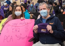 couple with sign: "Low pay makes PCA Shortage" indoors