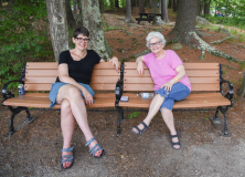 two women enjoying sitting on bench in woods