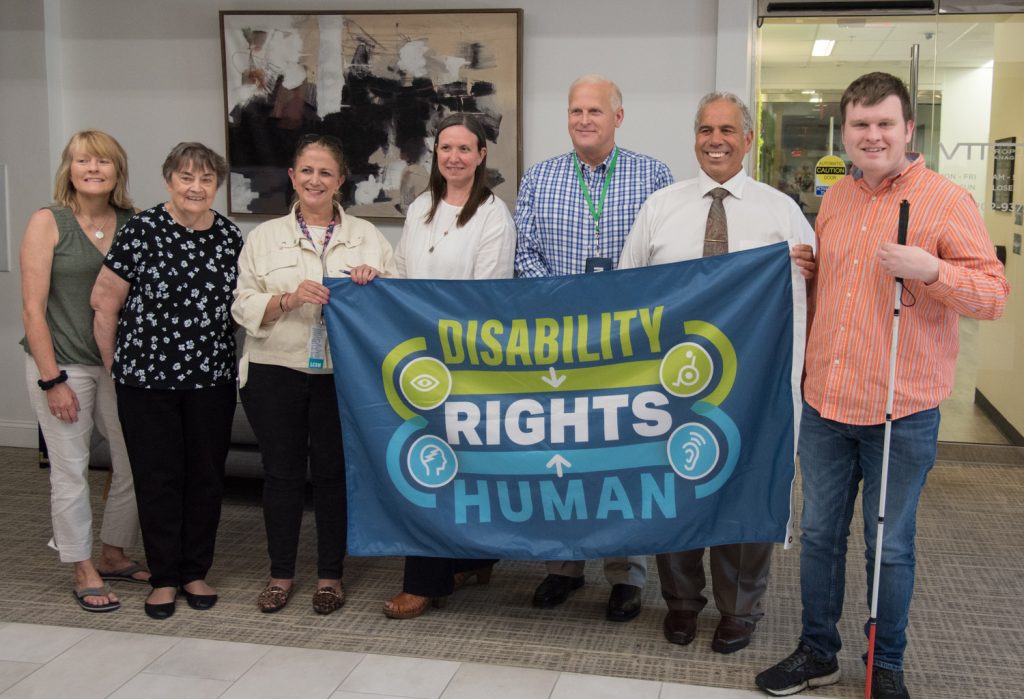 Staff and community members hold flag saying disability rights human rights.  This flag will be flown at Framingham City Hall