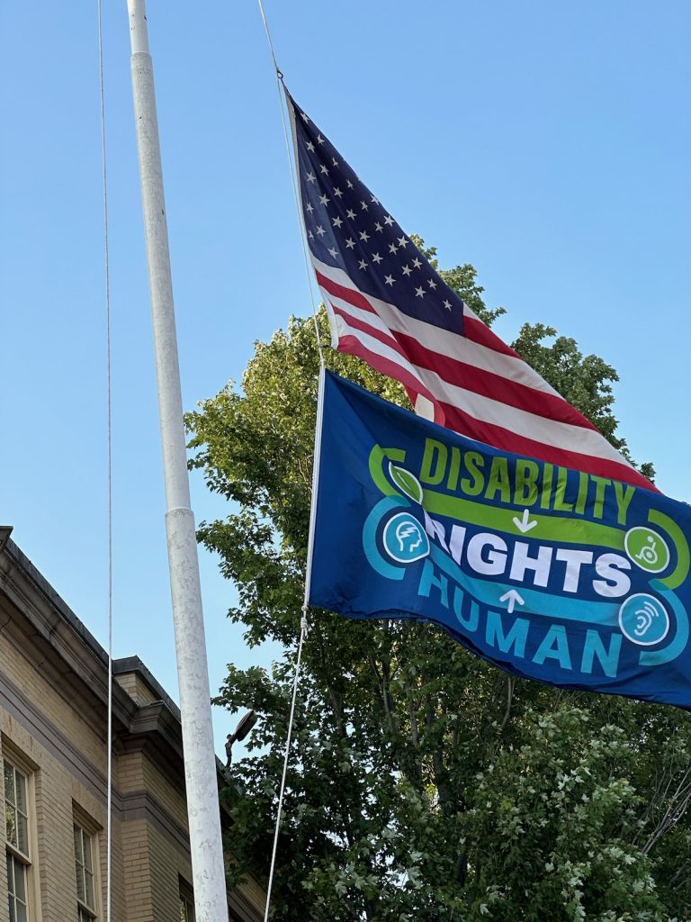 American flag on top, with Disability Human Rights flag directly under, flying at Memorial Building