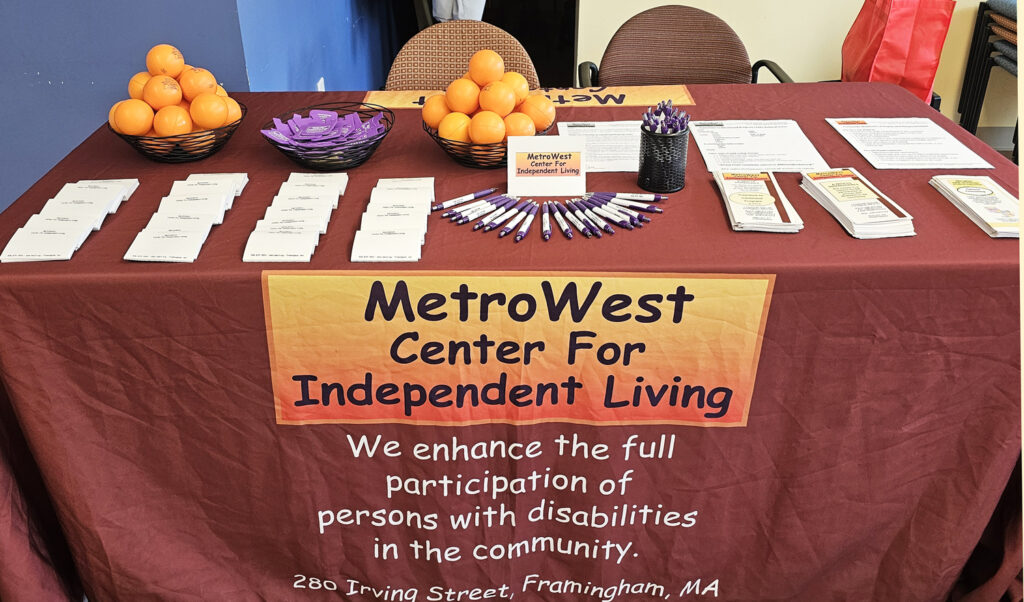 The MWCIL Options Counseling table with orange squeeze balls, pens, more swag and informational brochures. 